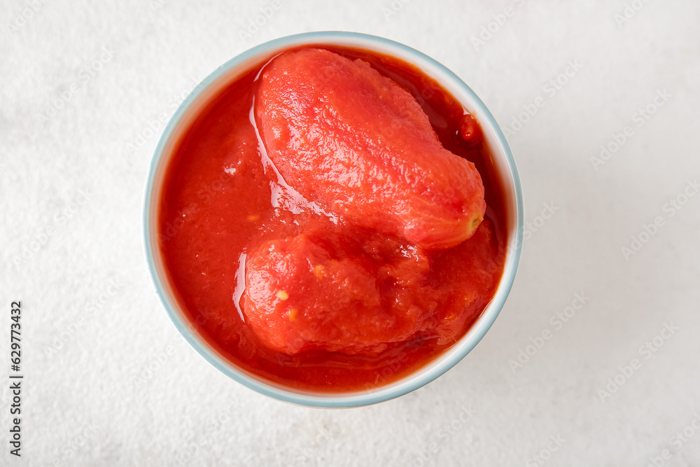 Bowl with canned tomatoes on light background