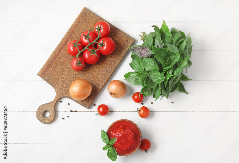 Composition with canned, fresh tomatoes, onion and basil on light wooden background