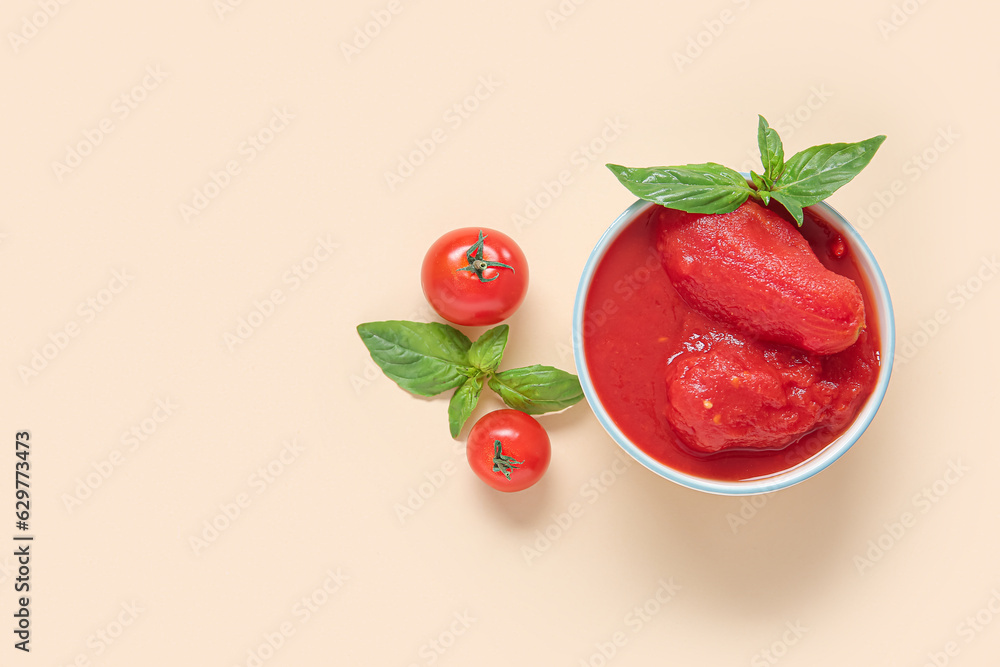 Bowl of tasty canned tomatoes and basil on color background