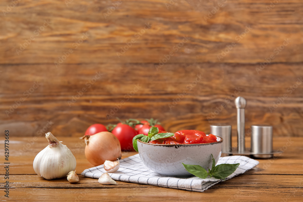 Bowl of canned tomatoes and spices on wooden background