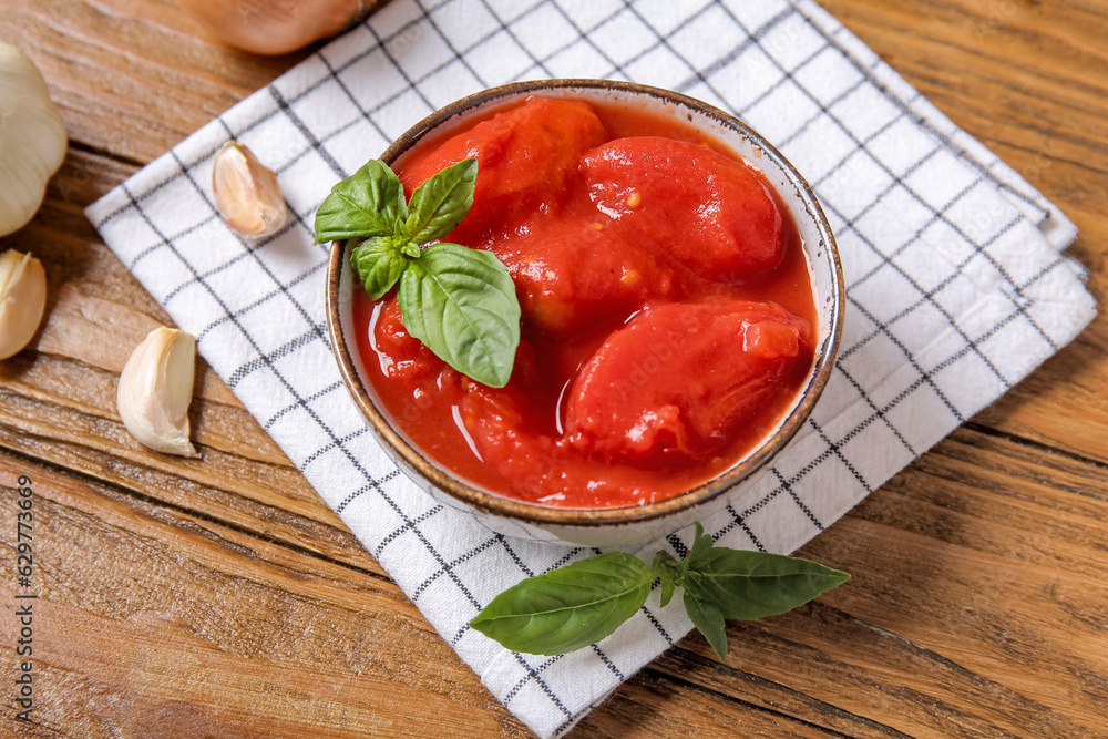 Bowl of tasty canned tomatoes and napkin on wooden background