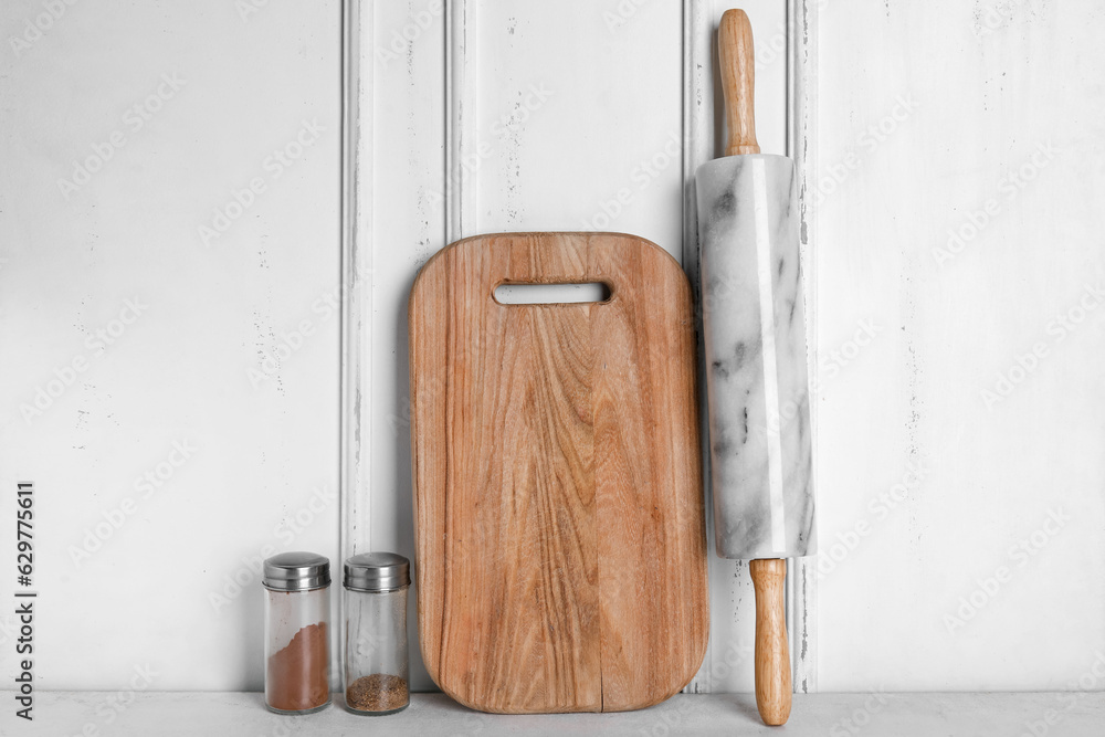 Wooden cutting board, rolling pin and spices on light background