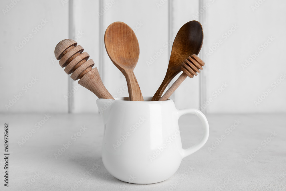 Ceramic pitcher with wooden kitchen tools on light background