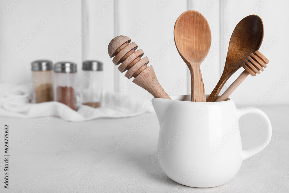 Ceramic pitcher with wooden kitchen tools on light background