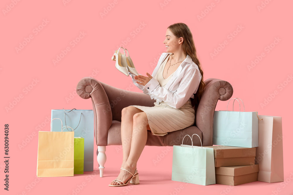 Young woman with stylish shoes in armchair on pink background