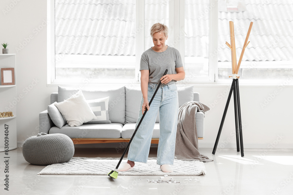 Mature woman sweeping floor in room