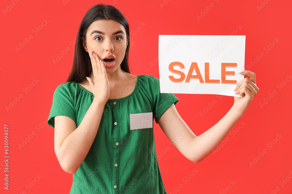 Shocked female seller with sale sign on red background