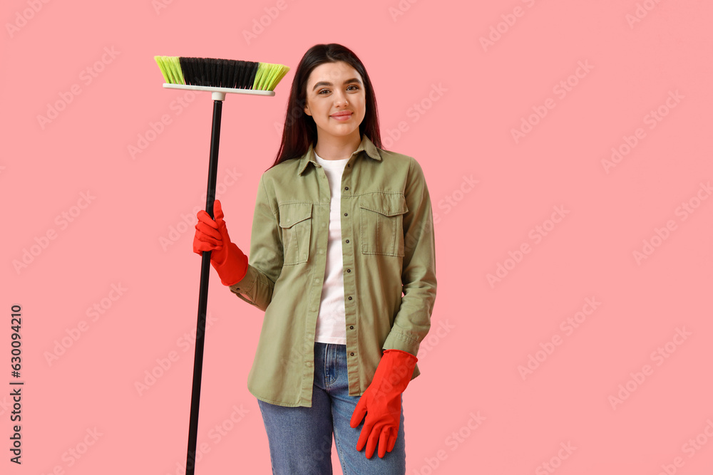 Young woman with broom on pink background