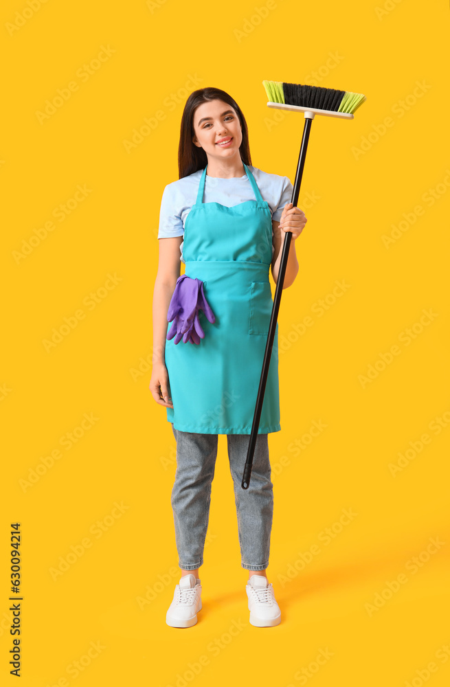 Female janitor with broom on yellow background