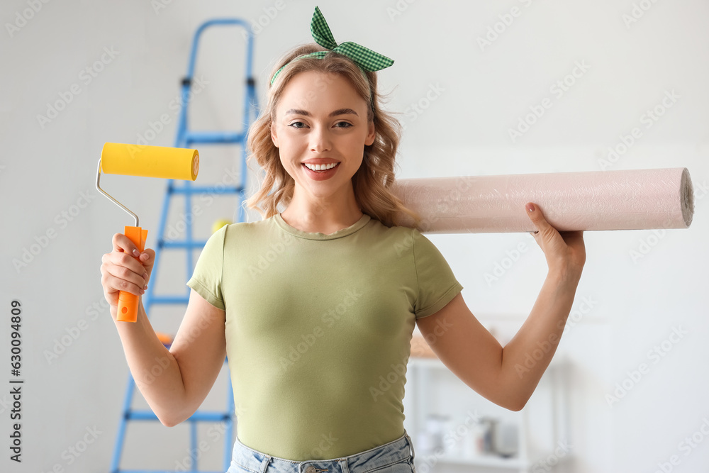 Young woman with wallpaper roll and paint roller at home