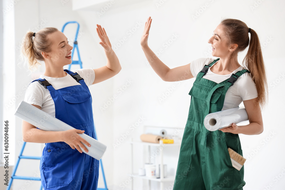 Female decorators with wallpaper rolls giving each other high-five in room