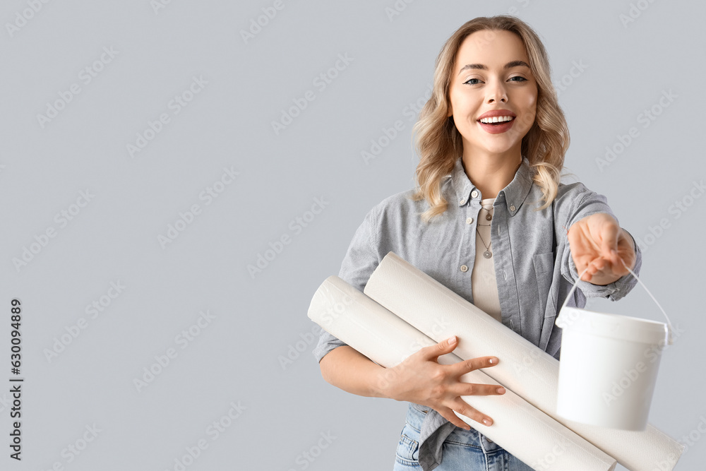 Young woman with wallpaper rolls and glue on grey background