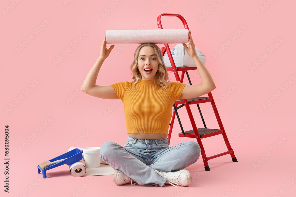 Happy young woman with wallpaper roll on pink background