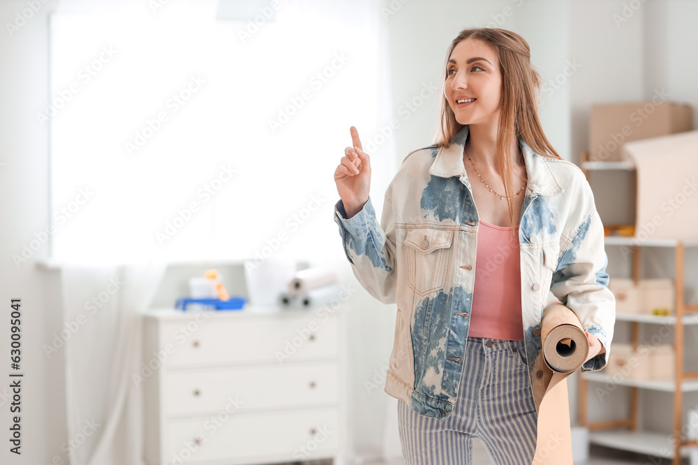 Young woman with wallpaper roll pointing at something in room