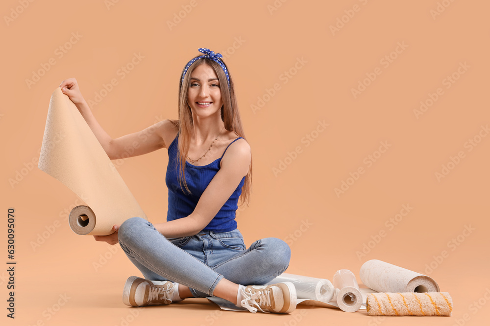 Young woman with wallpaper roll sitting on beige background