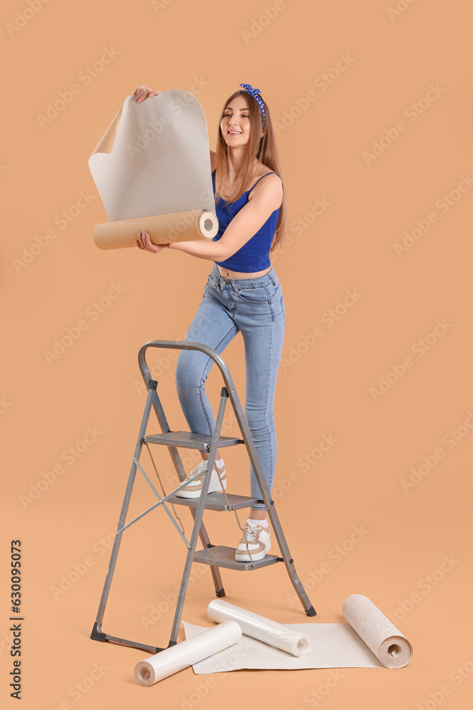 Young woman with wallpaper roll on ladder against beige background