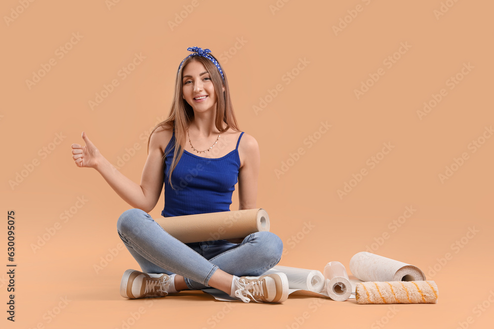 Young woman with wallpaper roll showing thumb-up on beige background