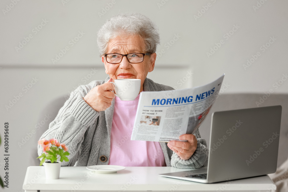 Senior woman with newspaper drinking coffee at home