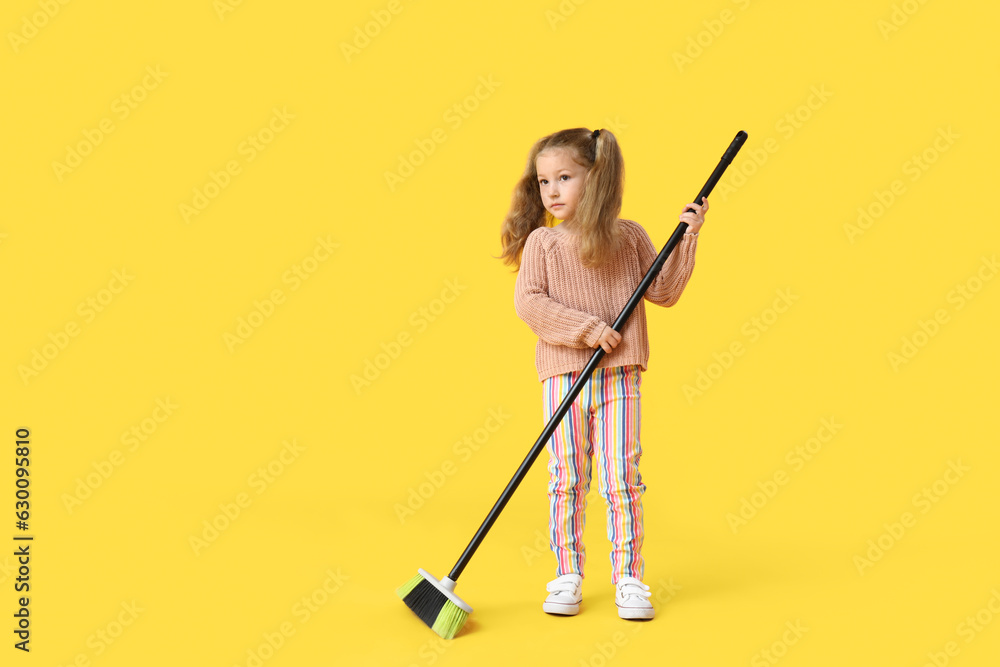 Cute little girl sweeping with broom on yellow background