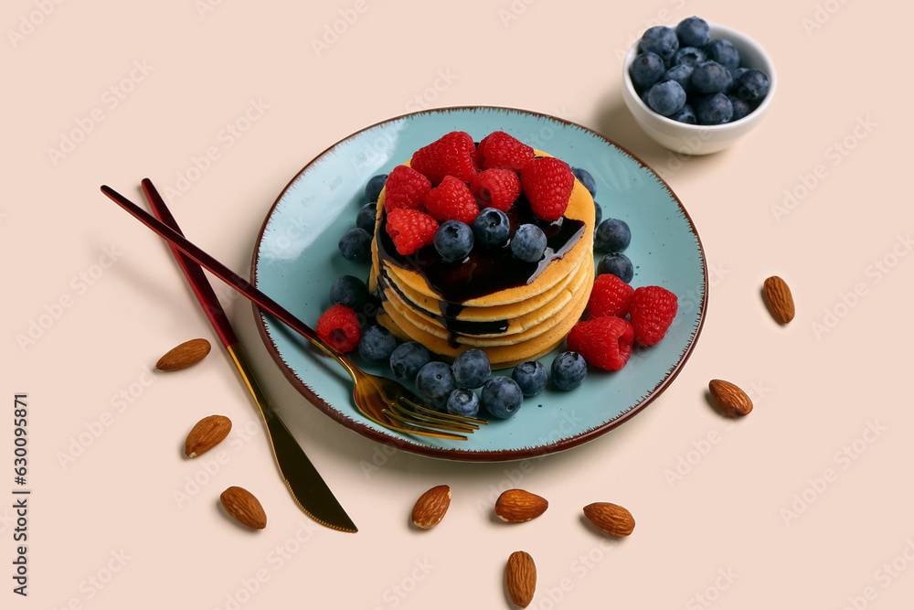 Plate with sweet pancakes, berries and nuts on beige background