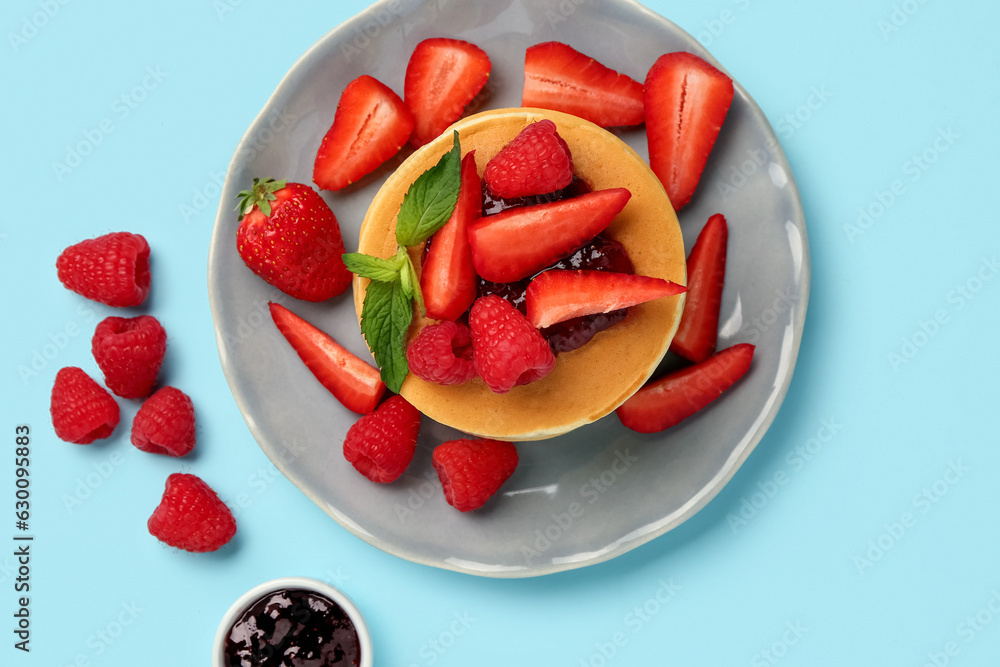 Plate with sweet pancakes, berries and jam on blue background