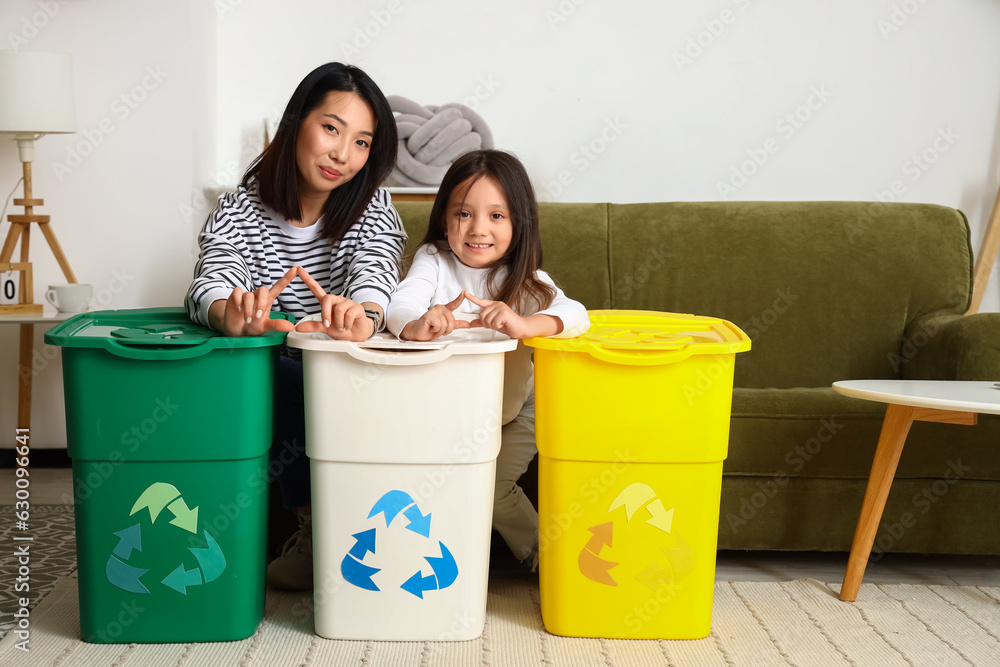 Asian mother with her little daughter and recycle bins at home