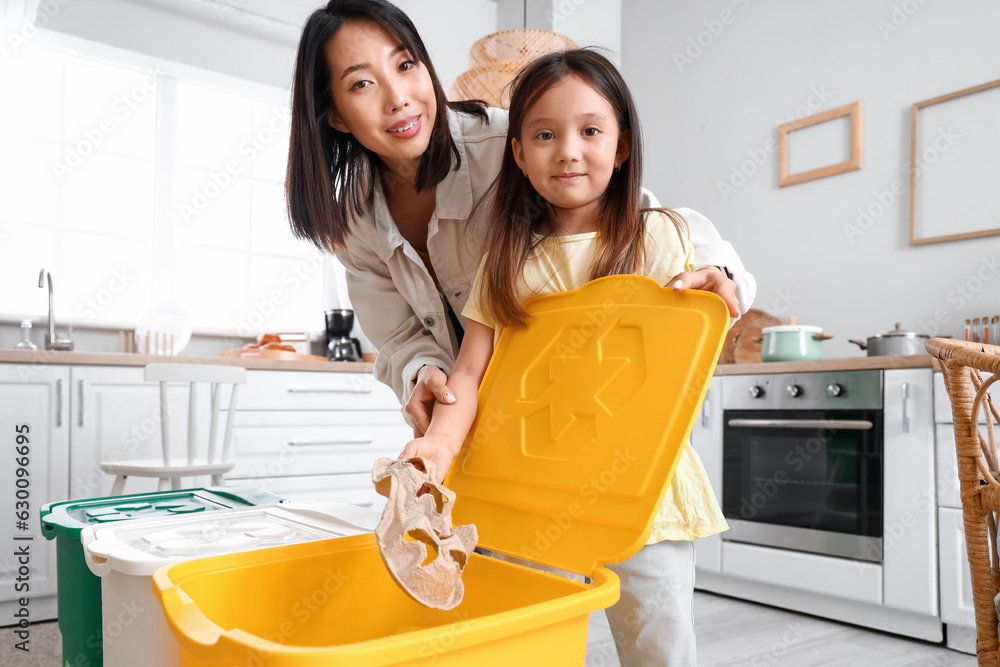 Asian mother with her little daughter throwing paper garbage in recycle bin at home