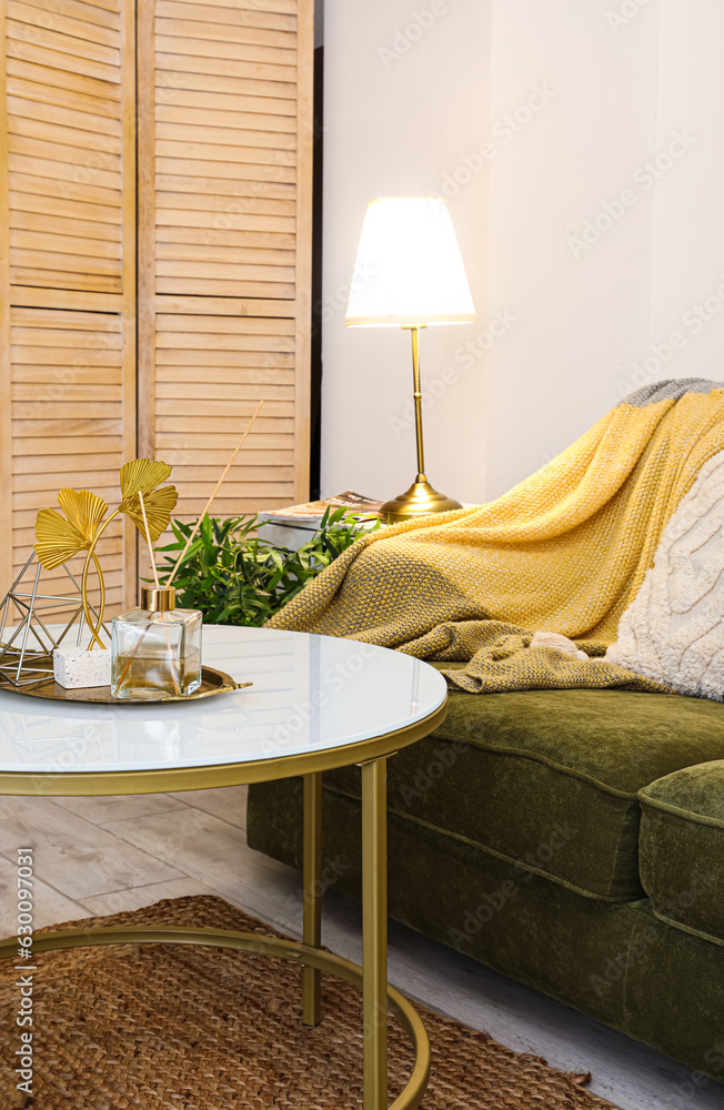 Interior of stylish living room with cozy green sofa, coffee table and glowing lamp