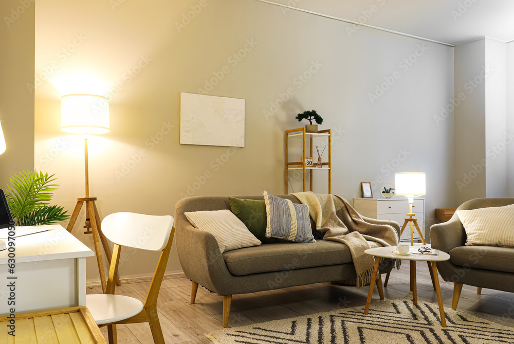 Interior of living room with grey sofa, armchair and glowing lamps