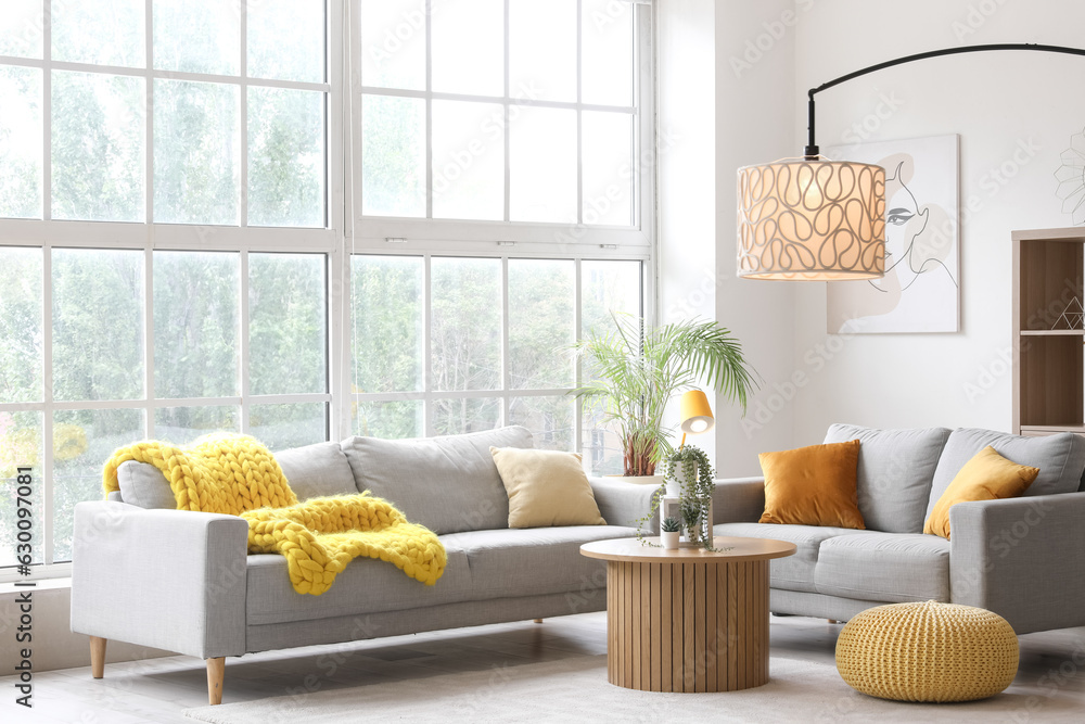 Interior of light living room with cozy grey sofas, coffee table and glowing lamps near big window