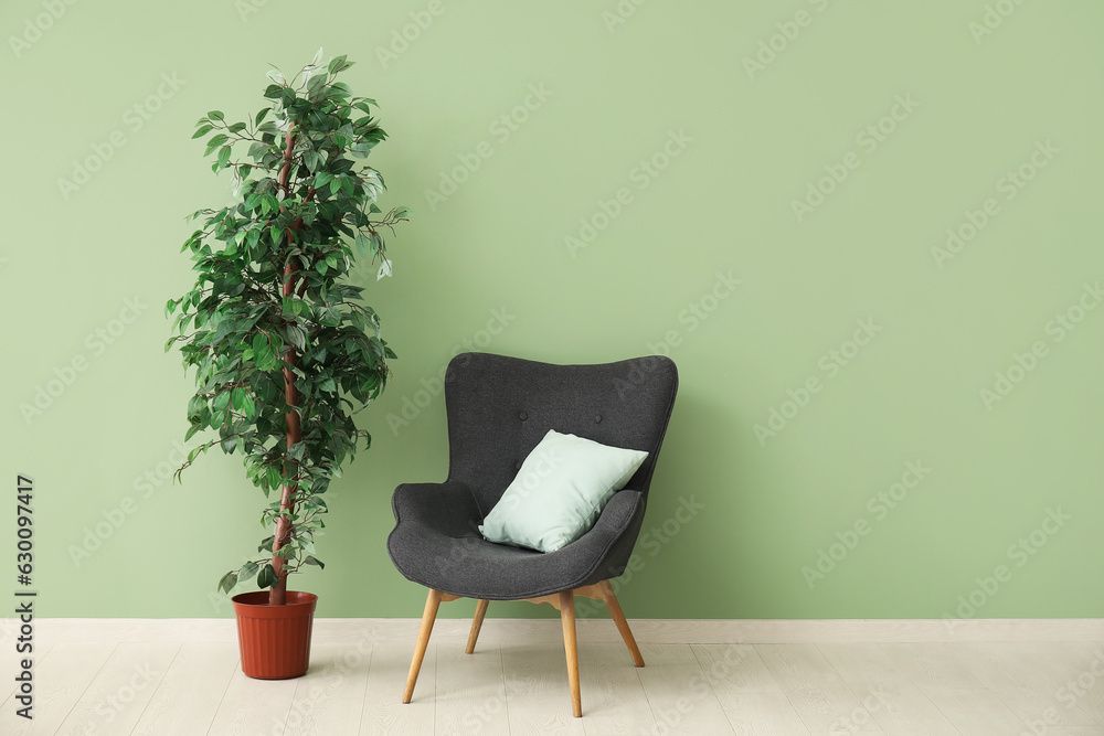 Dark grey armchair with pillow and houseplant near green wall