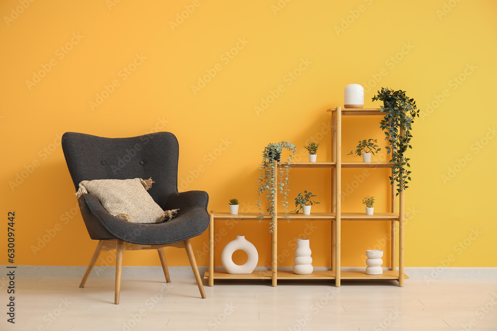 Dark grey armchair with pillow, shelving unit and houseplants near orange wall