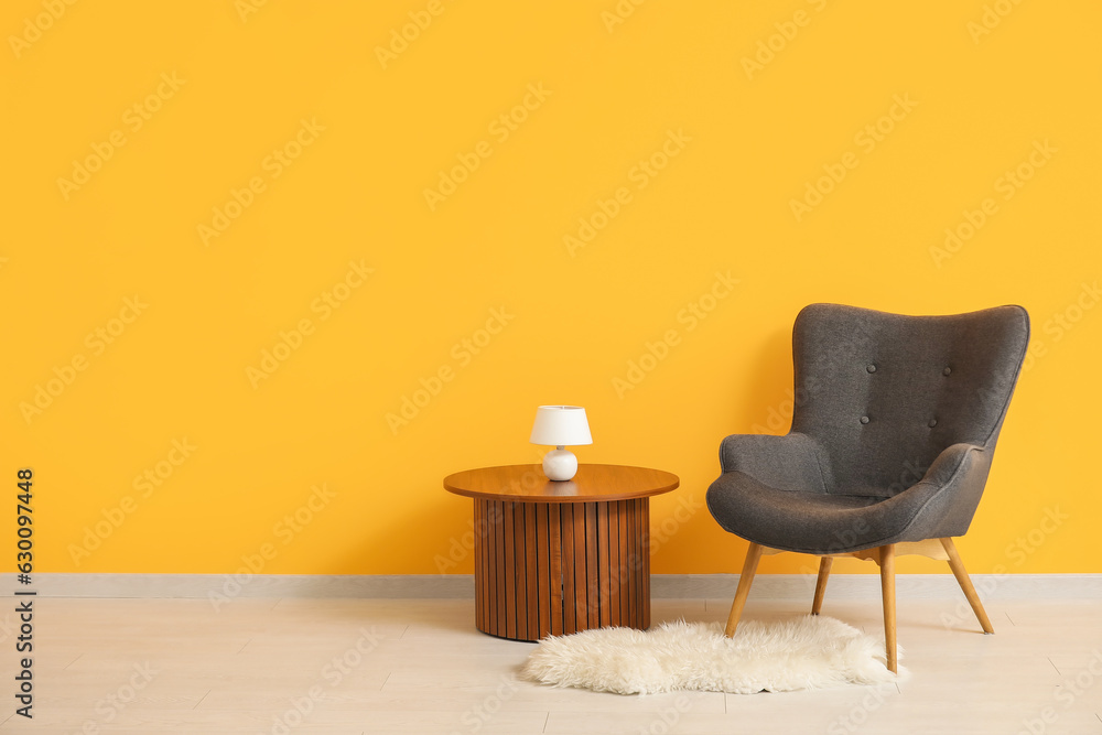 Dark grey armchair with wooden coffee table, lamp and fluffy rug near orange wall