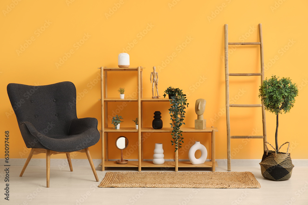 Dark grey armchair with shelving unit, houseplants and ladder near orange wall