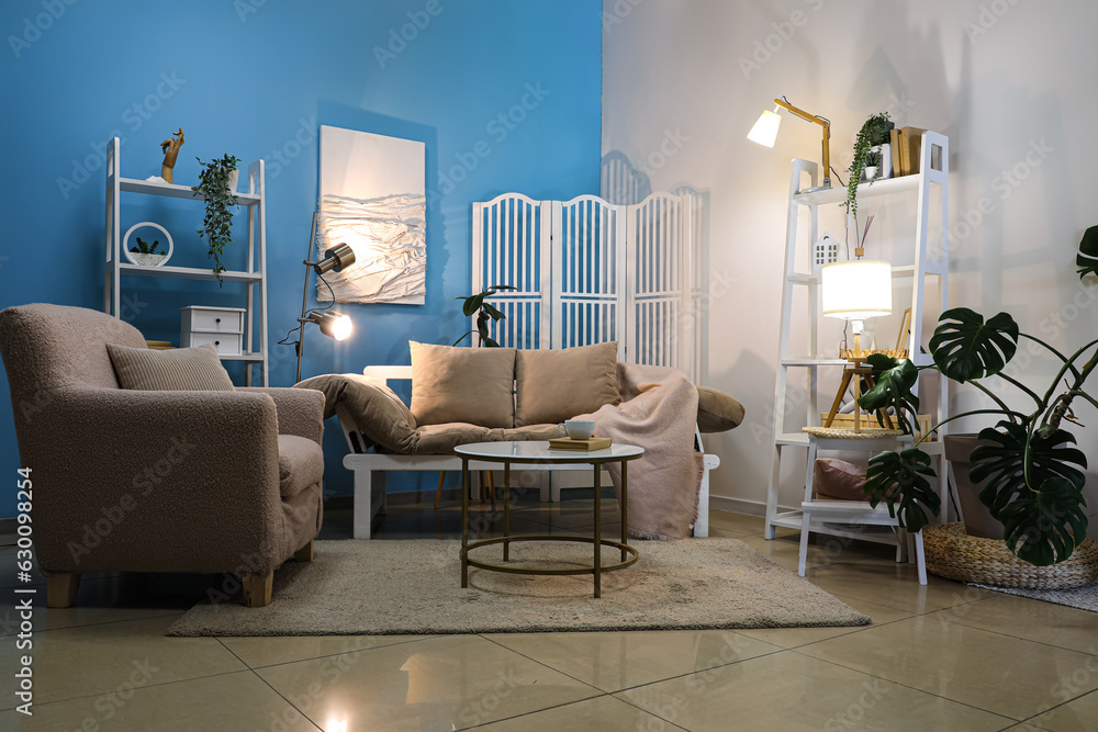 Interior of living room with glowing lamps, sofa and armchair