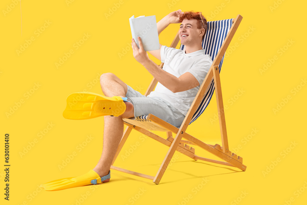 Young man reading book in deck chair on yellow background