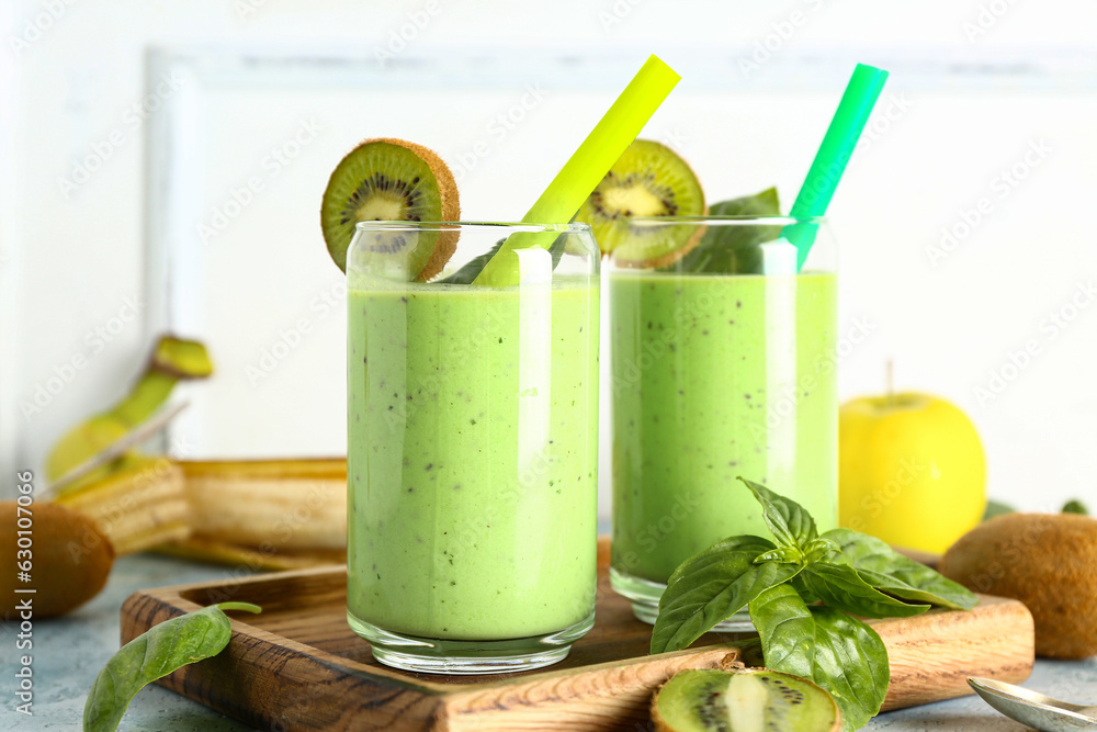 Glasses of fresh kiwi smoothie with basil on blue table