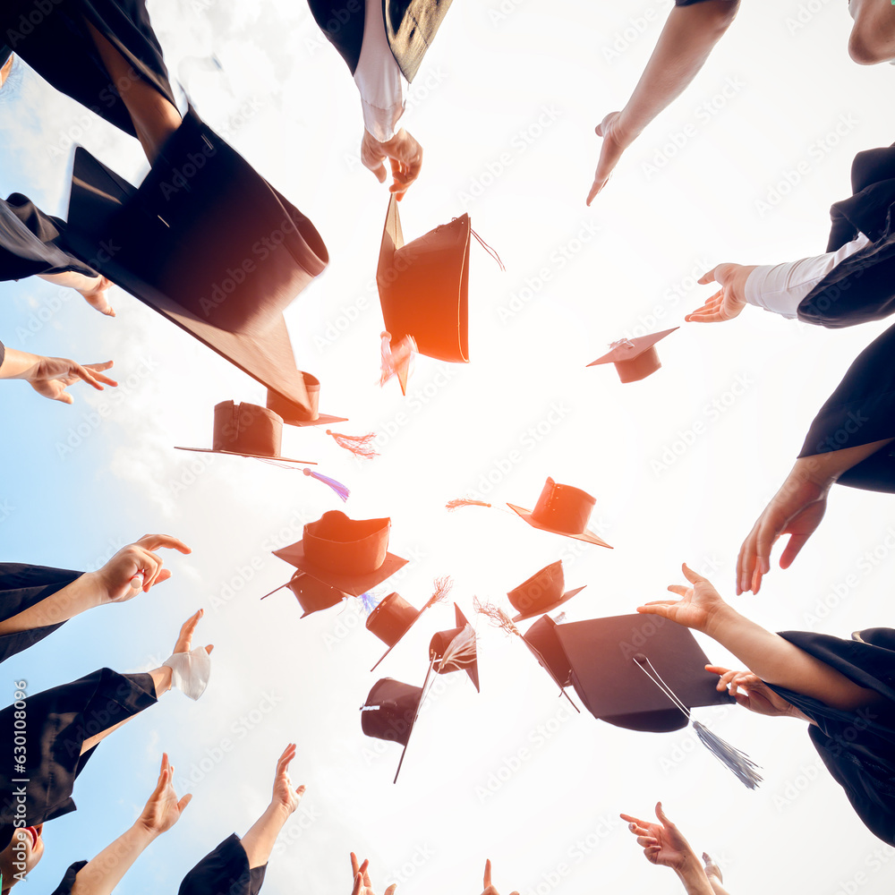 cheerful graduates in black gowns Graduation Caps Thrown in blue summer sky