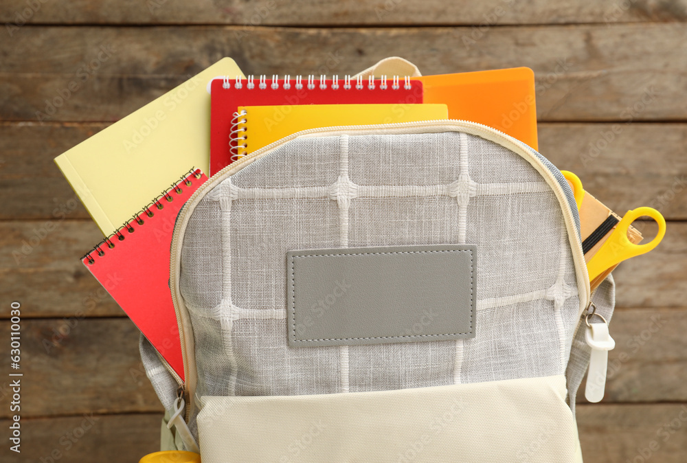 Grey school backpack with notebooks and scissors on wooden background