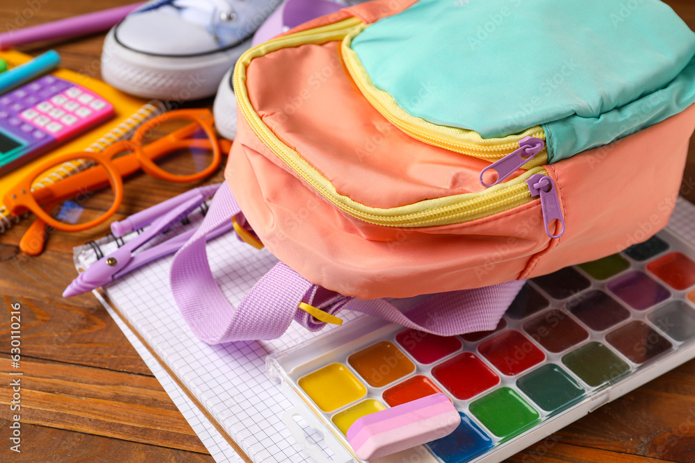 Colorful school backpack with eyeglasses, watercolors and different stationery on wooden table