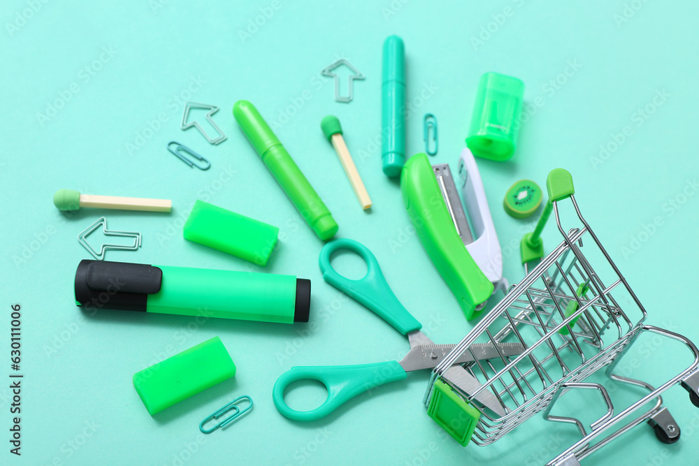 Shopping cart with different stationery on turquoise background