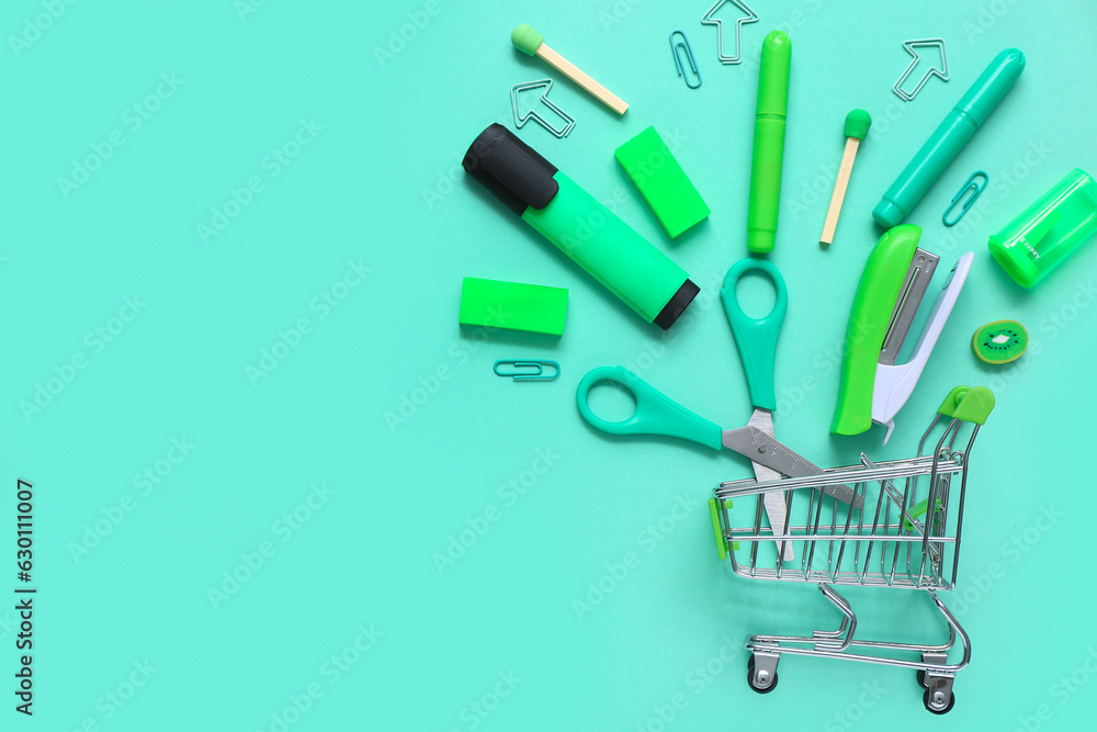 Shopping cart with different stationery on turquoise background