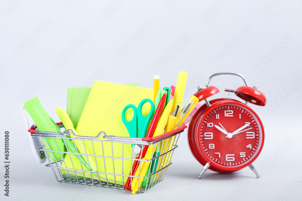 Alarm clock and shopping basket with different stationery on white background