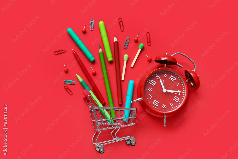 Alarm clock and shopping cart with different stationery on red background