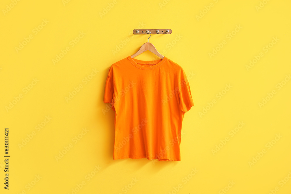 Stylish orange t-shirt hanging on yellow background