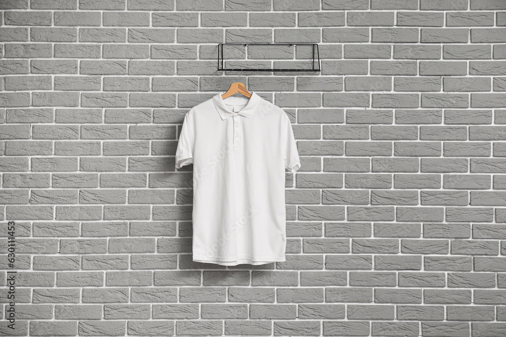 Stylish white t-shirt hanging on grey brick wall