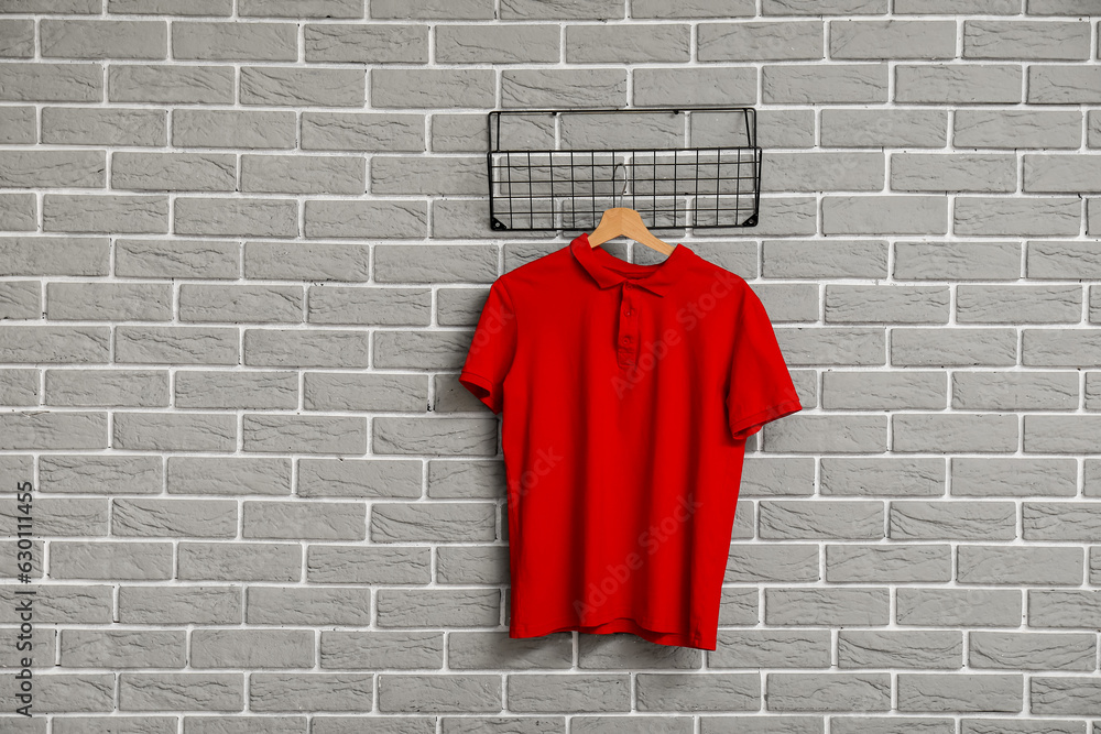 Stylish red t-shirt hanging on grey brick wall