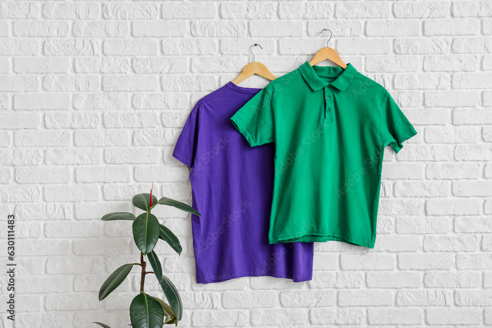 Stylish t-shirts hanging on white brick wall