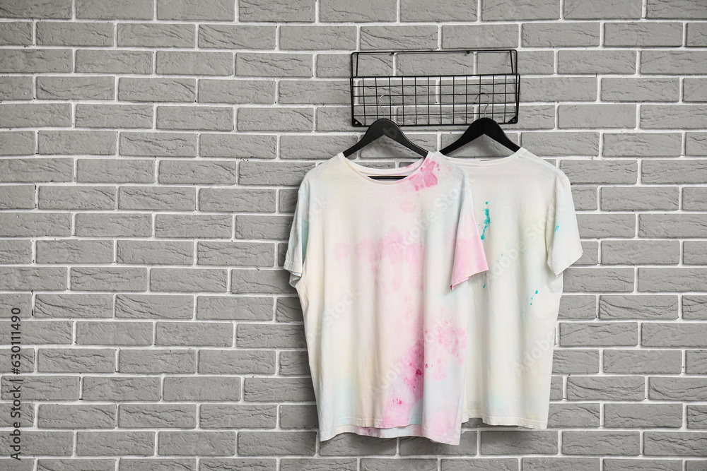 Stylish white t-shirts hanging on grey brick wall