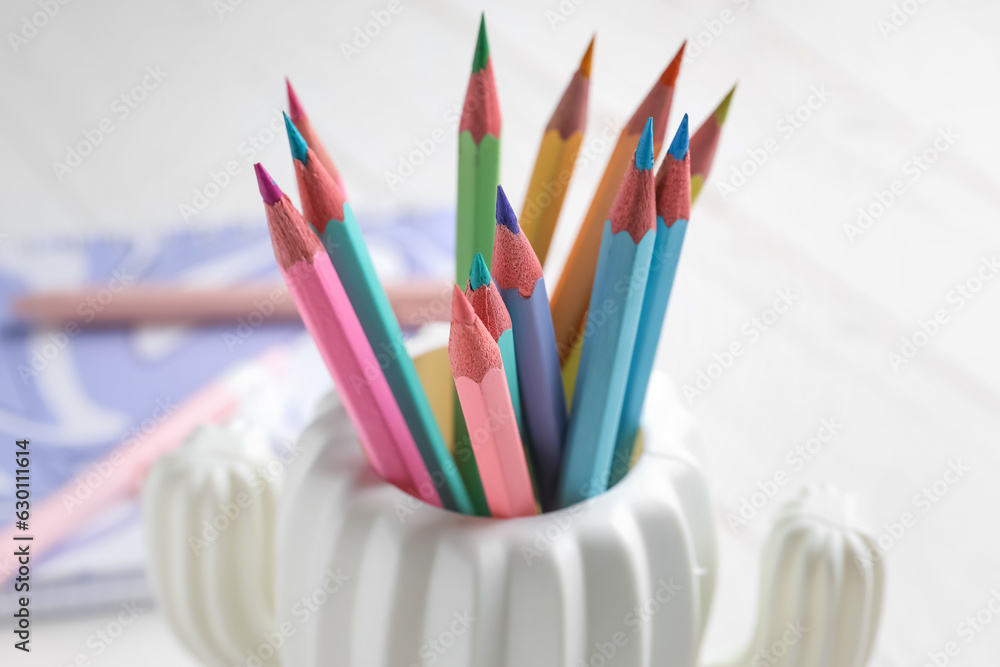 Stylish holder with different color pencils on light table, closeup